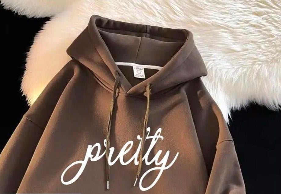 Brown hoodie with 'pretty' text on a fluffy white surface